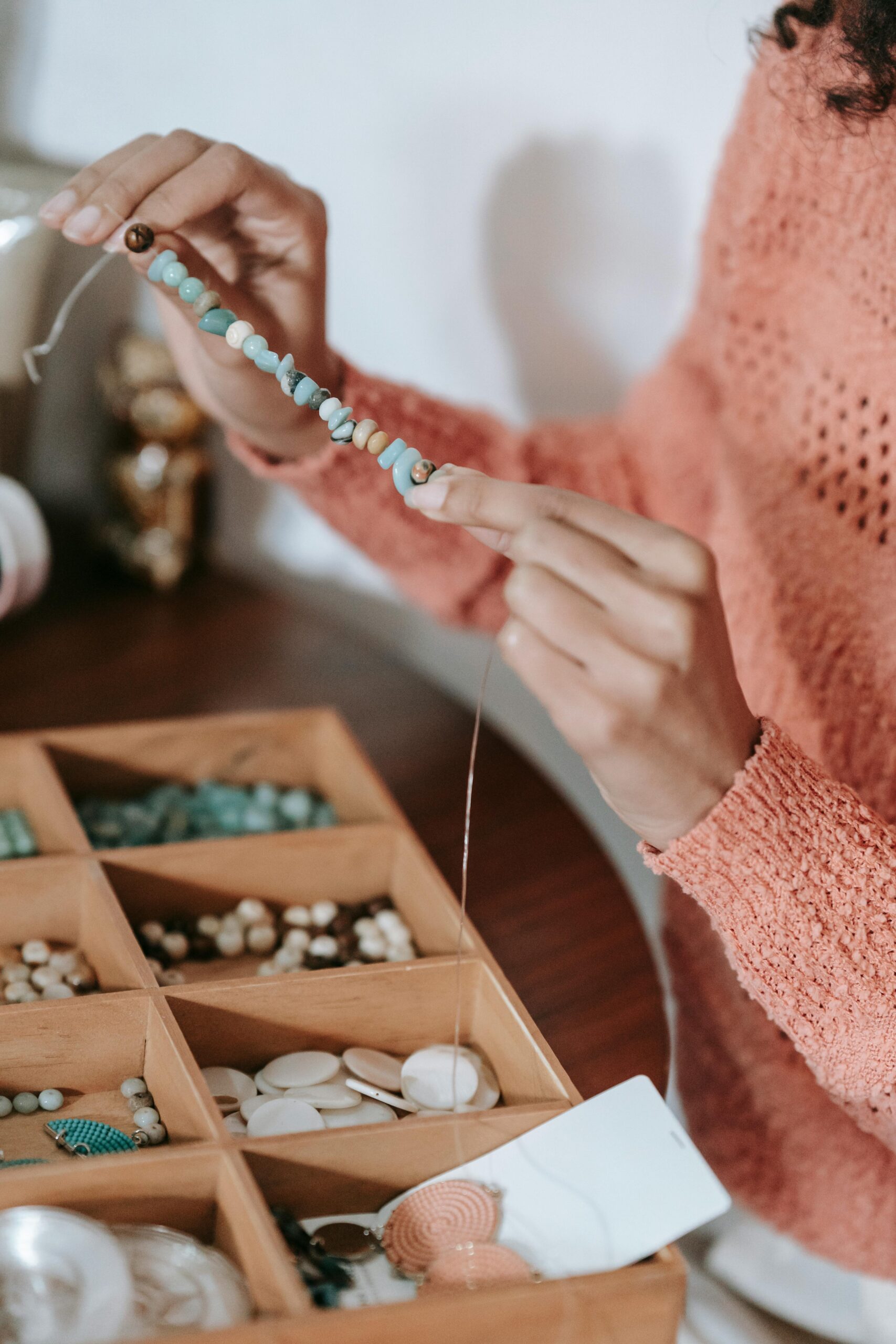 Crop unrecognizable craftswoman in casual clothes sitting at table with box for craftwork and demonstrating partly finished colorful decorative handmade accessory