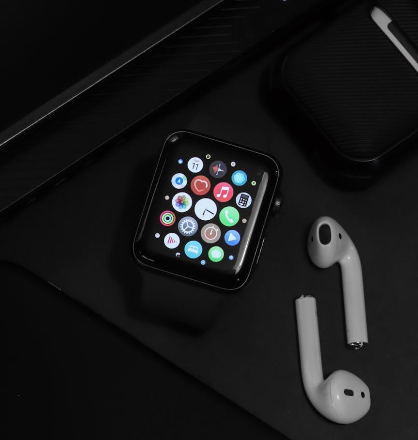Stylish arrangement of modern tech gadgets on a dark surface, showcasing an Apple watch and AirPods.